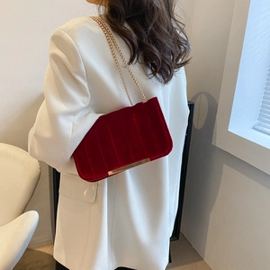 Sac bandoulière élégant en velours bordeaux avec chaîne dorée sur une veste blanche