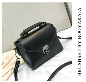 Detail view of black PU leather handbag with round metal clasp and adjustable strap