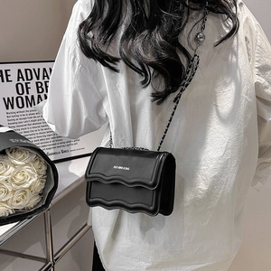 Minimalist black wave-edge flap bag with silver chain strap shown on a model