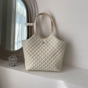 Detail shot of a quilted off-white tote bag featuring a golden floral metal plaque decoration