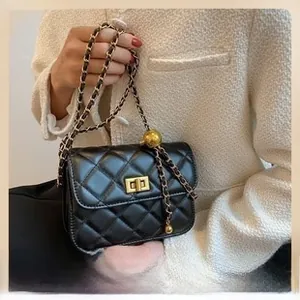 Detail of black quilted leather shoulder bag with gold ball accent and chain strap