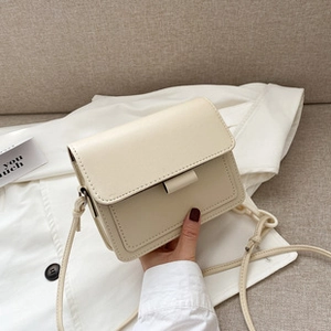 Detail view of cream square bag with flap closure, fine stitching, and thin shoulder strap