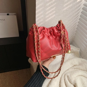 Detail of red quilted crossbody bag with golden chain strap in elegant indoor setting