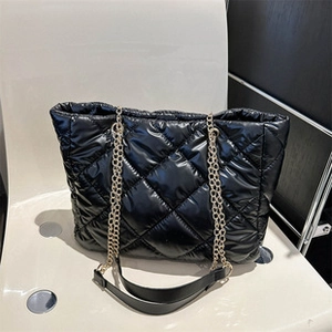 Close-up of black quilted down tote bag with golden chain and glossy nylon texture