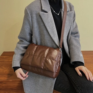 Detail of dark brown quilted puffer crossbody bag worn with a wool coat