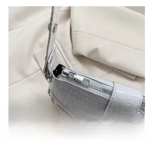 Detailansicht einer weißen Handtasche mit Krokodilmuster und silbernem Metallreißverschluss