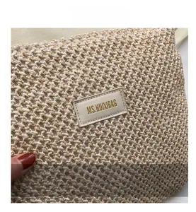 Detailed close-up of woven texture and stitched brand logo on beige crossbody tote bag