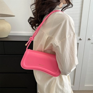 Pink leather underarm shoulder bag with gold hardware shown on a model from a side view
