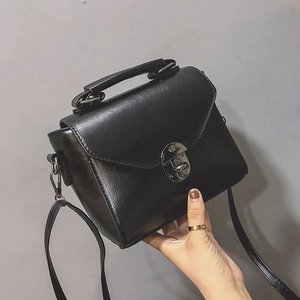 Close-up of black leather crossbody bag with silver buckle and hand-held details