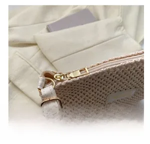 Close-up of beige woven tote bag showing smooth gold zipper and white leather strap
