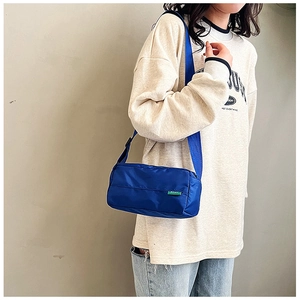 Dettaglio di una borsa a tracolla in nylon blu navy indossata da una modella con etichetta