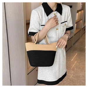 Detail of woven straw tote bag with khaki and black color blocks held by a model