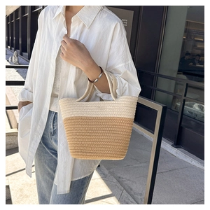 Detail of a two-tone woven straw bucket bag with white and beige contrast stitching