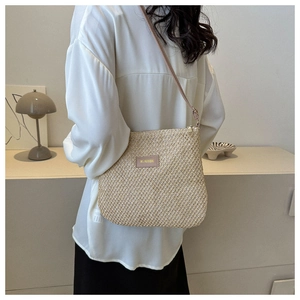 Detail showing woven straw crossbody bag with leather logo patch worn by a model