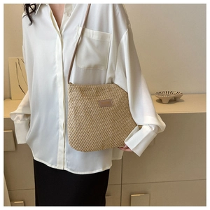 Detailed close-up of a beige straw woven tote bag featuring a leather SHINING label
