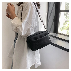 Close-up of black lychee grain leather crossbody bag with silver zipper and wide strap