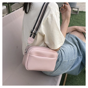 Pink crossbody camera bag with wide fabric strap shown in a lifestyle outdoor setting