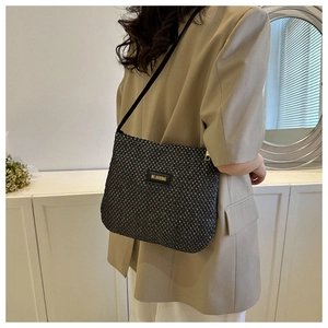 Detail of black woven crossbody bag texture with gold metal logo worn with a beige blazer