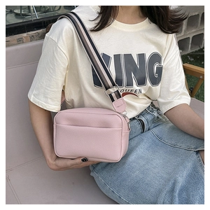 Detail of pink crossbody bag showing litchi texture and striped wide fabric strap