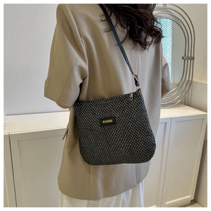 Detailed view of black woven shoulder bag with logo patch on beige suit outfit