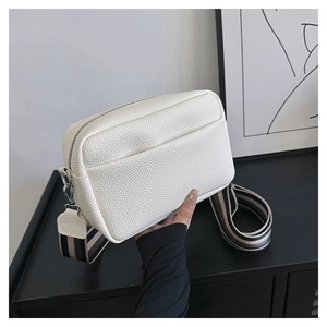 White pebbled leather crossbody bag with striped fabric strap shown in hand detail
