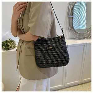 Detail of black woven shoulder bag with golden logo label worn over a beige blazer
