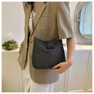 Detail of black woven shoulder bag featuring a rectangular brand label with golden lettering