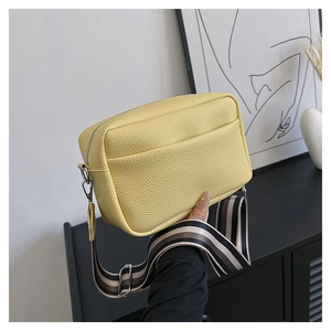Detail of yellow lychee grain leather crossbody bag with striped woven strap