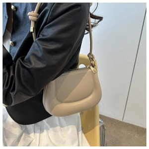 Close-up of a cream puffy underarm bag with knot strap detail and gold zipper finish