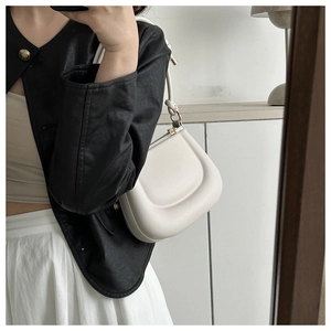 Close-up of a minimalist cream leather underarm bag with gold buckle on shoulder strap
