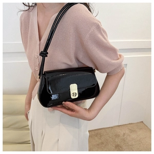 Detail of a black patent leather shoulder bag with a gold buckle worn by a model