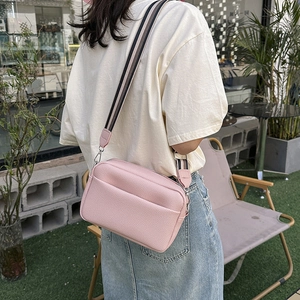 Pink litchi texture crossbody camera bag with adjustable striped strap on a female model