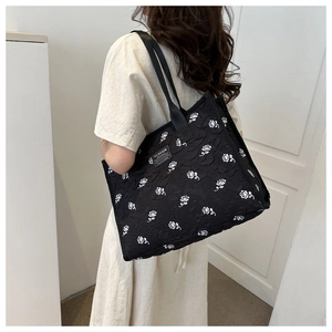 Close-up of a large black tote bag with white rose patterns worn by a model on shoulder