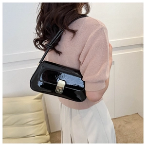 Model wearing black patent leather shoulder bag with gold clasp detail in sleek style