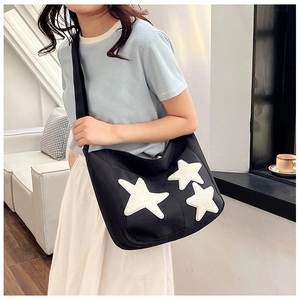 Detail shot of black canvas tote bag with plush white stars and adjustable shoulder strap