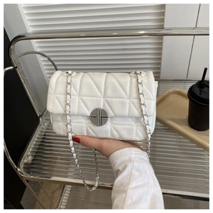 Detailed view of white quilted crossbody bag with silver rotary lock and metal chain strap