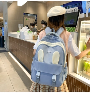 Rear view of a light blue student backpack with white buckle details in a cafe setting