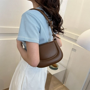 Minimalist brown leather shoulder bag with knot detail shown on model in a chic indoor setting