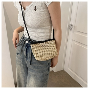 Close-up of a beige woven straw crossbody bag featuring a slim black shoulder strap