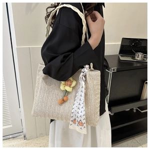 Detail of beige herringbone woven tote bag with flower charm and silk scarf decoration