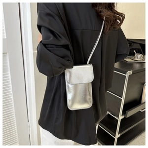 Detail of a minimalist silver metallic crossbody phone bag worn by a model