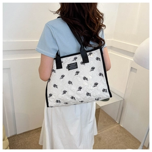 Close-up of a white quilted tote bag with black rose prints and a wide shoulder strap