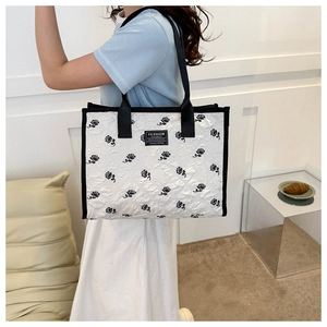 Detailed macro view of white quilted tote bag featuring black rose floral prints