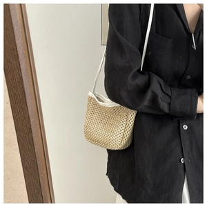 Close-up of beige woven straw bucket bag featuring white straps and mesh texture