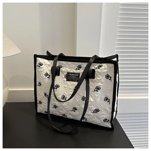 Detail view of the quilted rose pattern fabric and black logo on the large tote bag