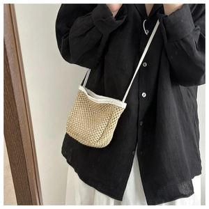 Detail of woven straw shoulder bag featuring white fabric trim and a slender strap