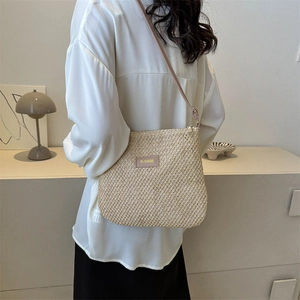 Minimalist beige woven straw crossbody bag with brown strap and leather patch