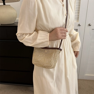 Minimalist beige straw bucket bag with brown leather trim worn with a white dress