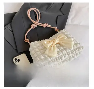 Detail der weißen Plissee-Tasche mit Seidenschleife und Größenvergleich zu einem Telefon