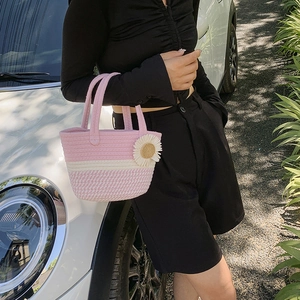 Pink and white woven bucket handbag with daisy charm held by a model next to a car
